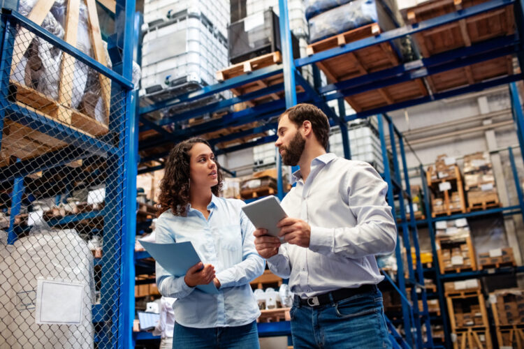 Manager with female colleague taking inventory in company warehouse. Warehouse employees checking stock levels in store room.