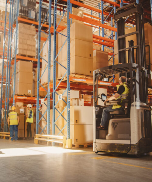 Retail Delivery Warehouse full of Shelves with Goods in Cardboard Boxes, Workers Scan and Sort Packages, Move Inventory with Pallet Trucks and Forklifts. Product Distribution and Delivery Logistics.