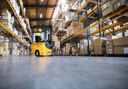 Young male worker lowering a pallet with boxes. Forklift driver working in a warehouse.