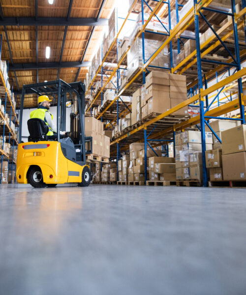 Young male worker lowering a pallet with boxes. Forklift driver working in a warehouse.