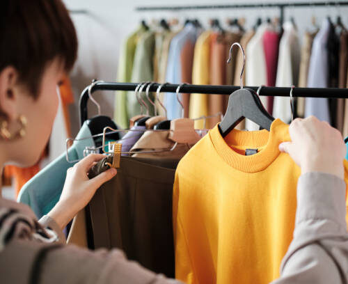 istockphoto-1338894509-612x612 Rear view of young woman looking at clothes on rack in her hands and choosing a new style for herself in the clothes store